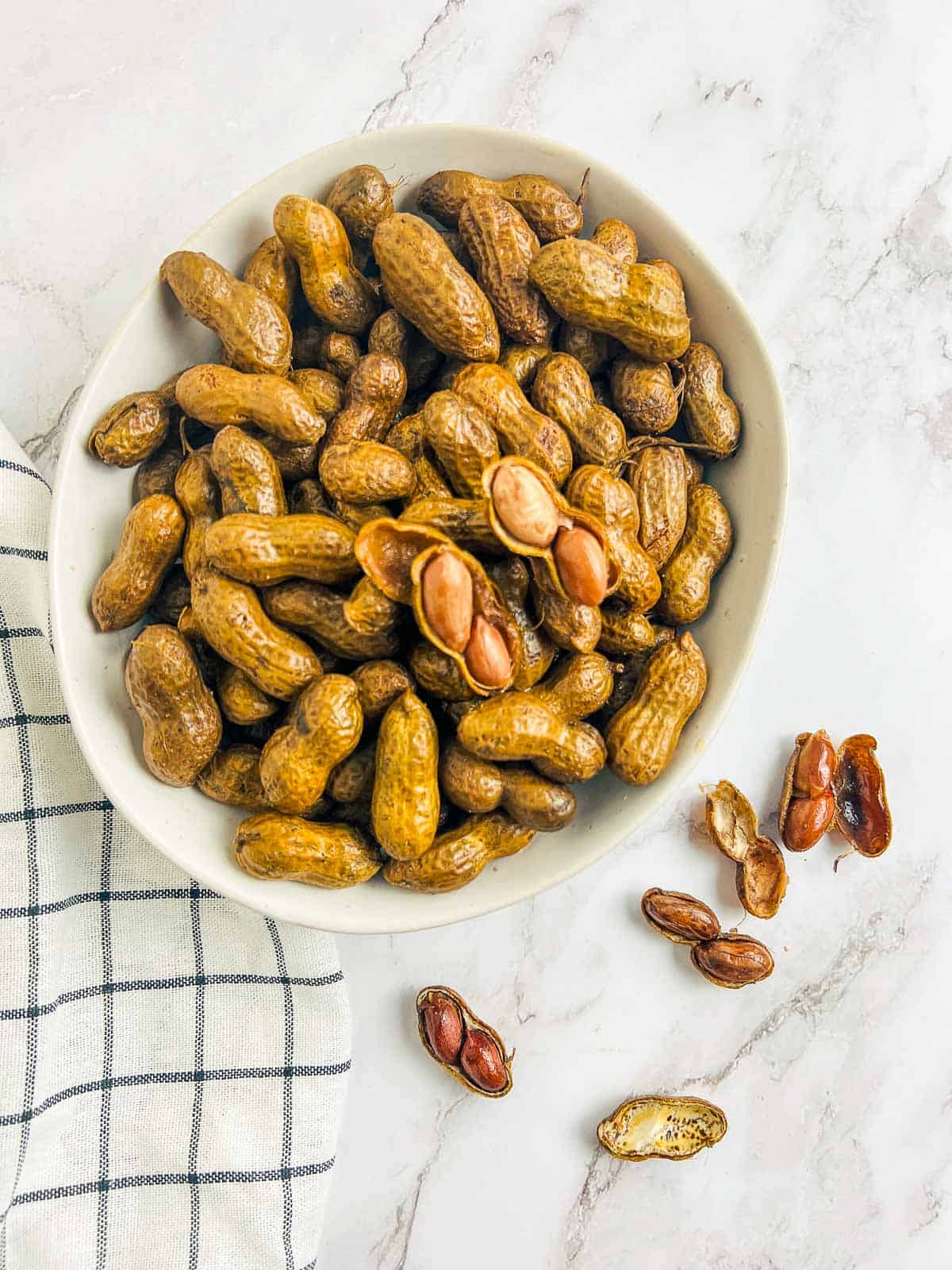 Boiled unshelled peanuts on a marble surface with a few peanuts out of shell.