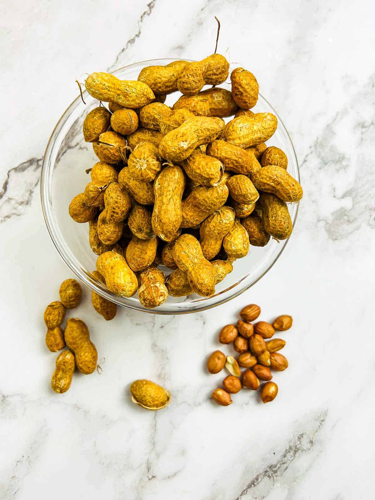 Shelled and unshelled raw peanuts on a marble surface.
