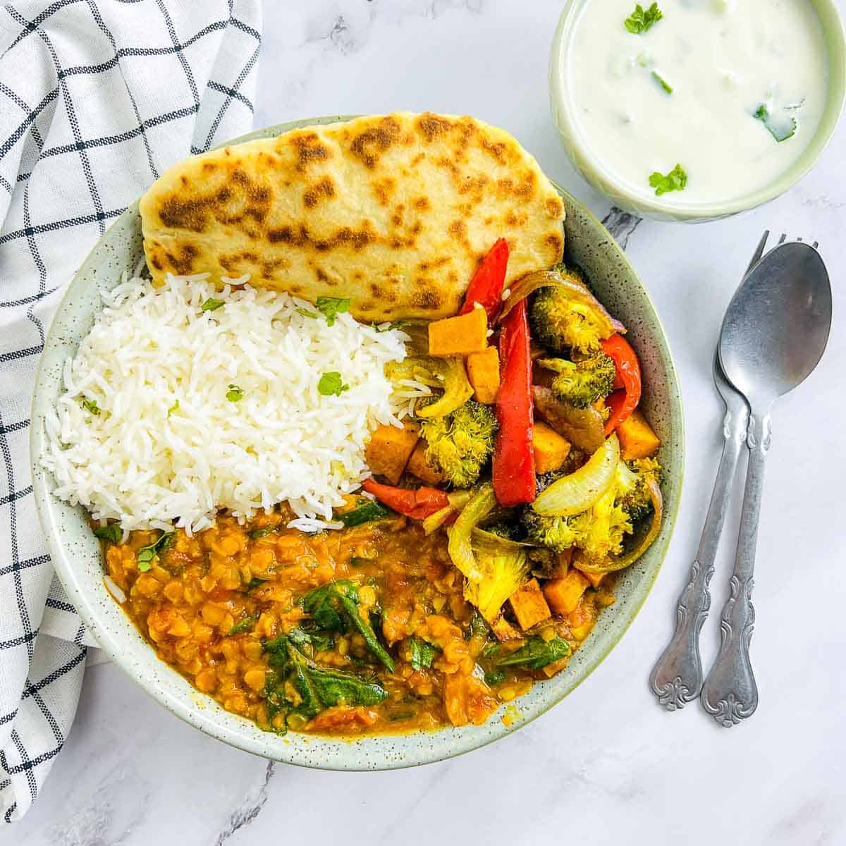 Red lentil dal Buddha bowl on a marble surface with raita in a separate bowl in the background.