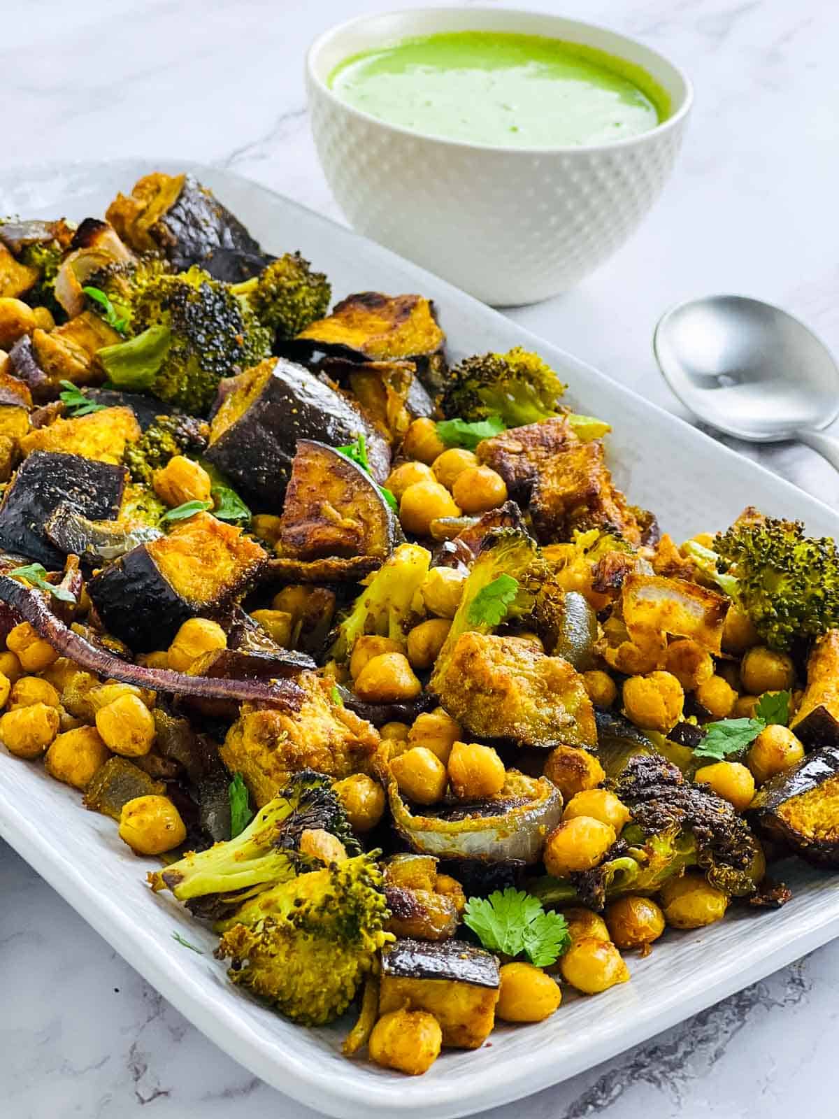 Side view of roasted veggies and chickpeas with mint yogurt sauce in the background.