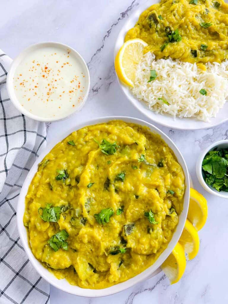 Zucchini dal in a white bowl with rice-dal plate and yogurt in the background.