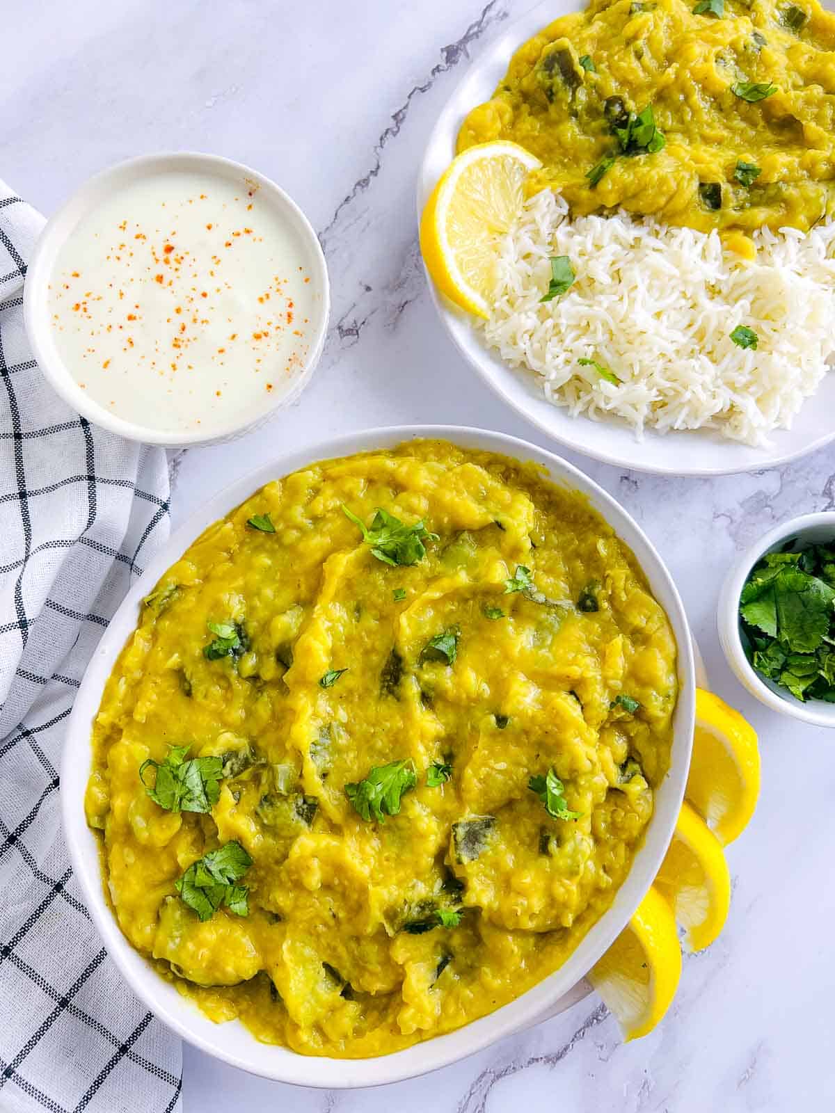 Zucchini dal in a white bowl with rice-dal plate and yogurt in the background.