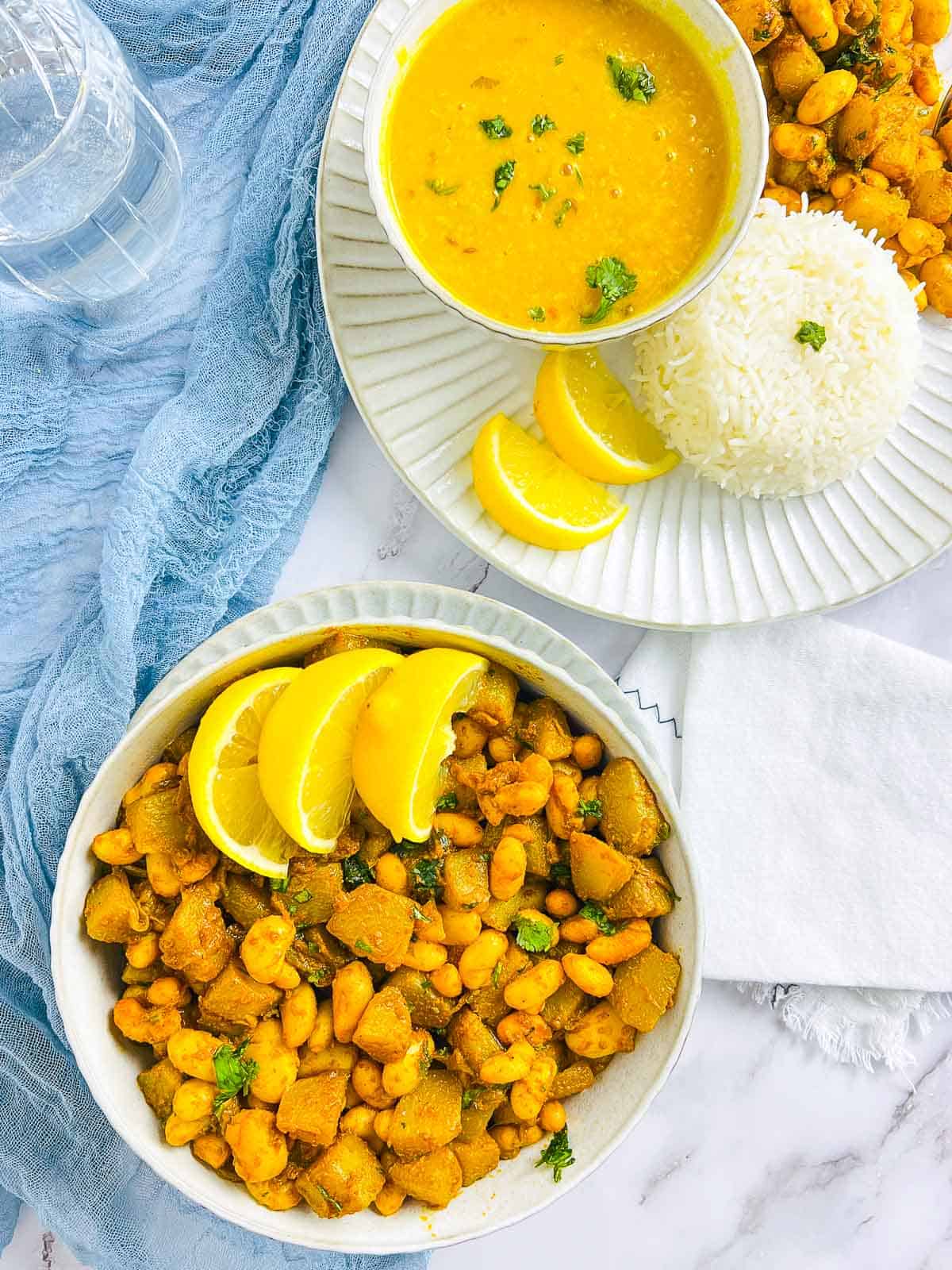Pan-fried chayote squash and white beans in a white bowl with a plate of dal and rice in the background.