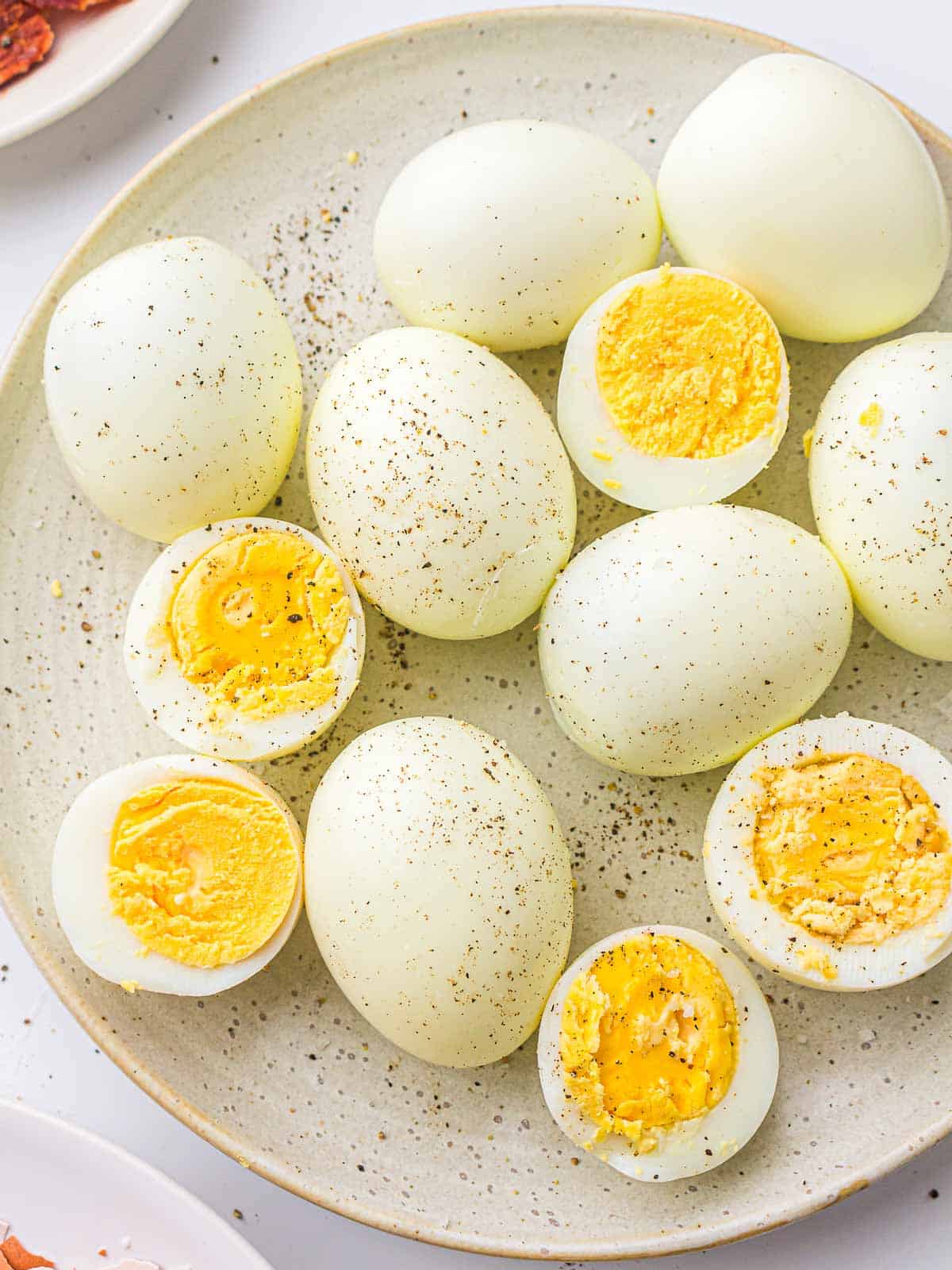 Boiled eggs seasoned with salt and pepper on a white plate.