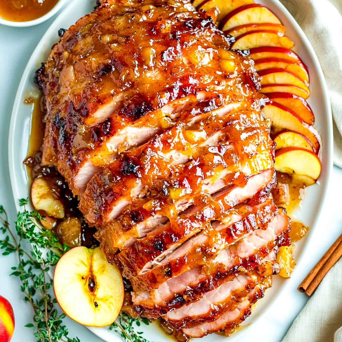 Apple cider glazed ham on a white plate garnished with roasted apple wedges.