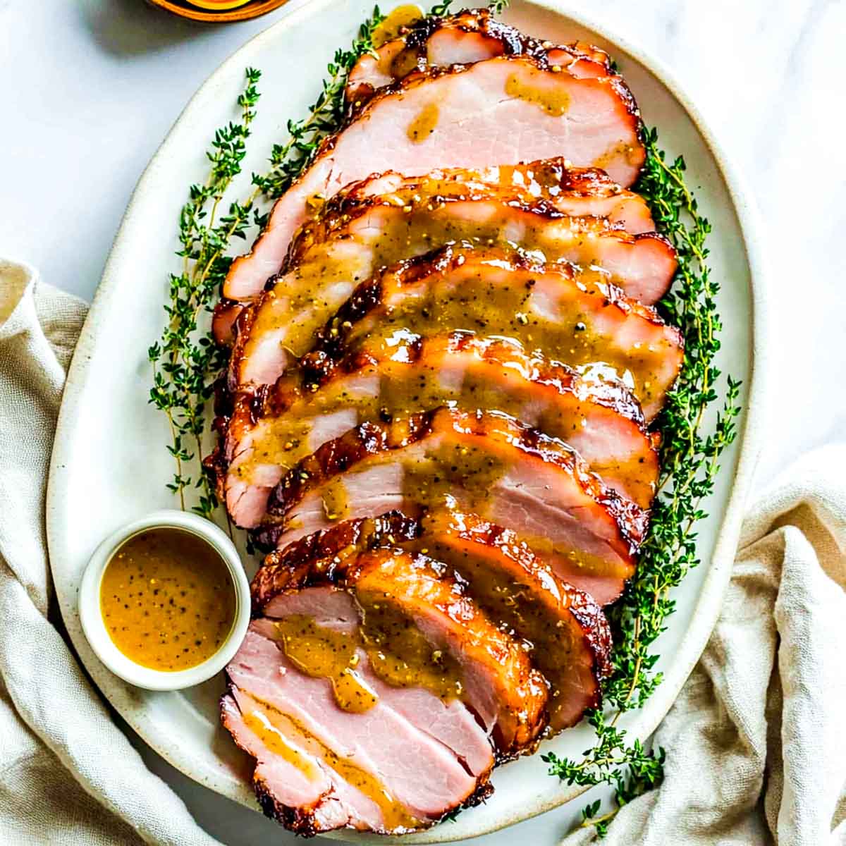 Dijon mustard glazed ham on a serving plate garnished with rosemary.