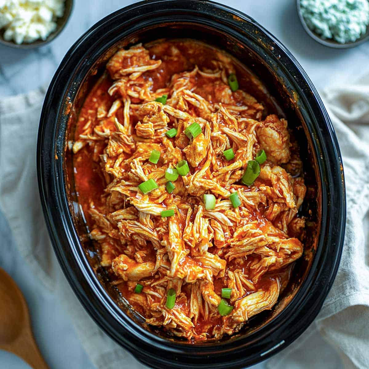Shredded buffalo chicken in crockpot with blue cheese in the background.