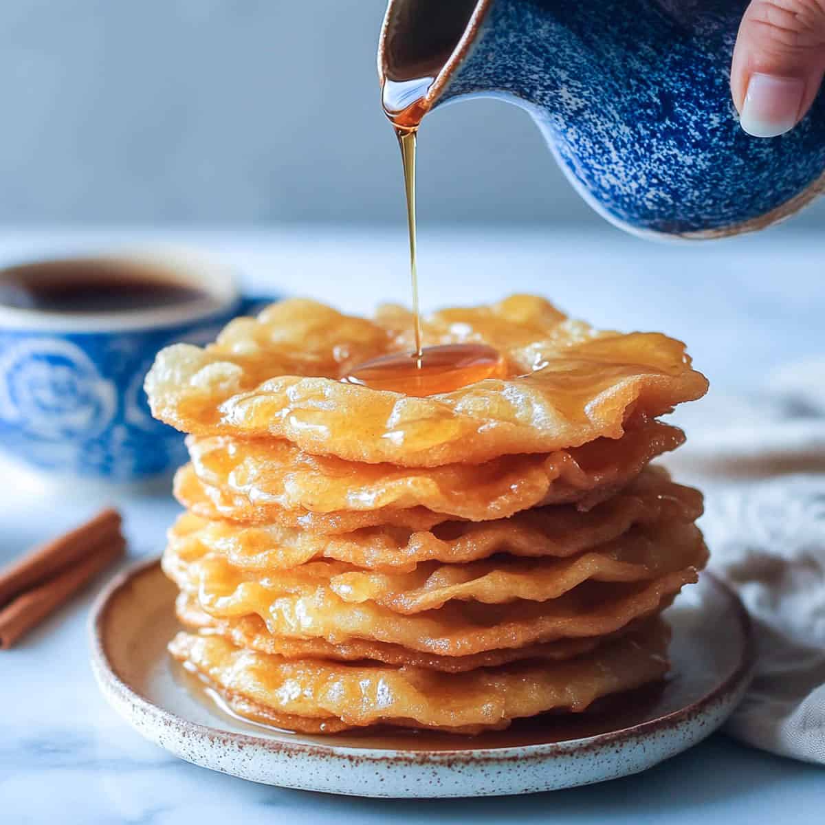 Bunuelos satck on a serving plate with syup being poured from top.