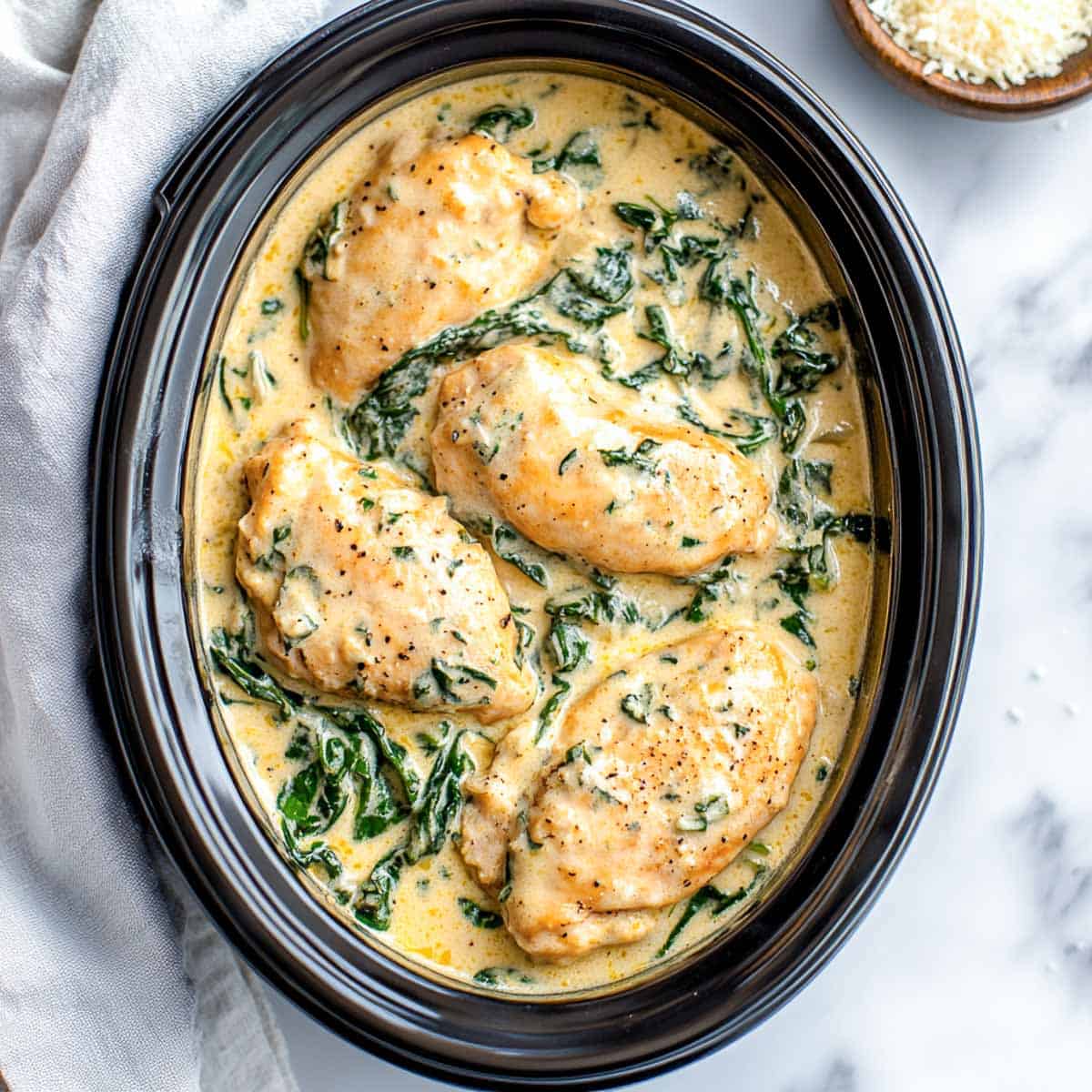 Creamy florentine chicken in crockpot placed on white marble surface.