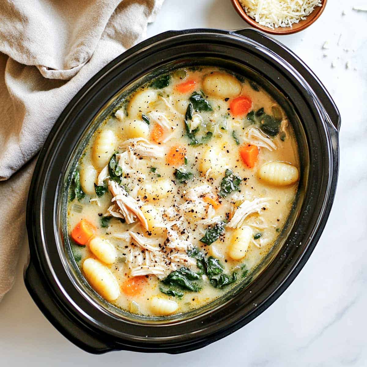 Creamy gnocchi soup with a bowl of cheese in the background.