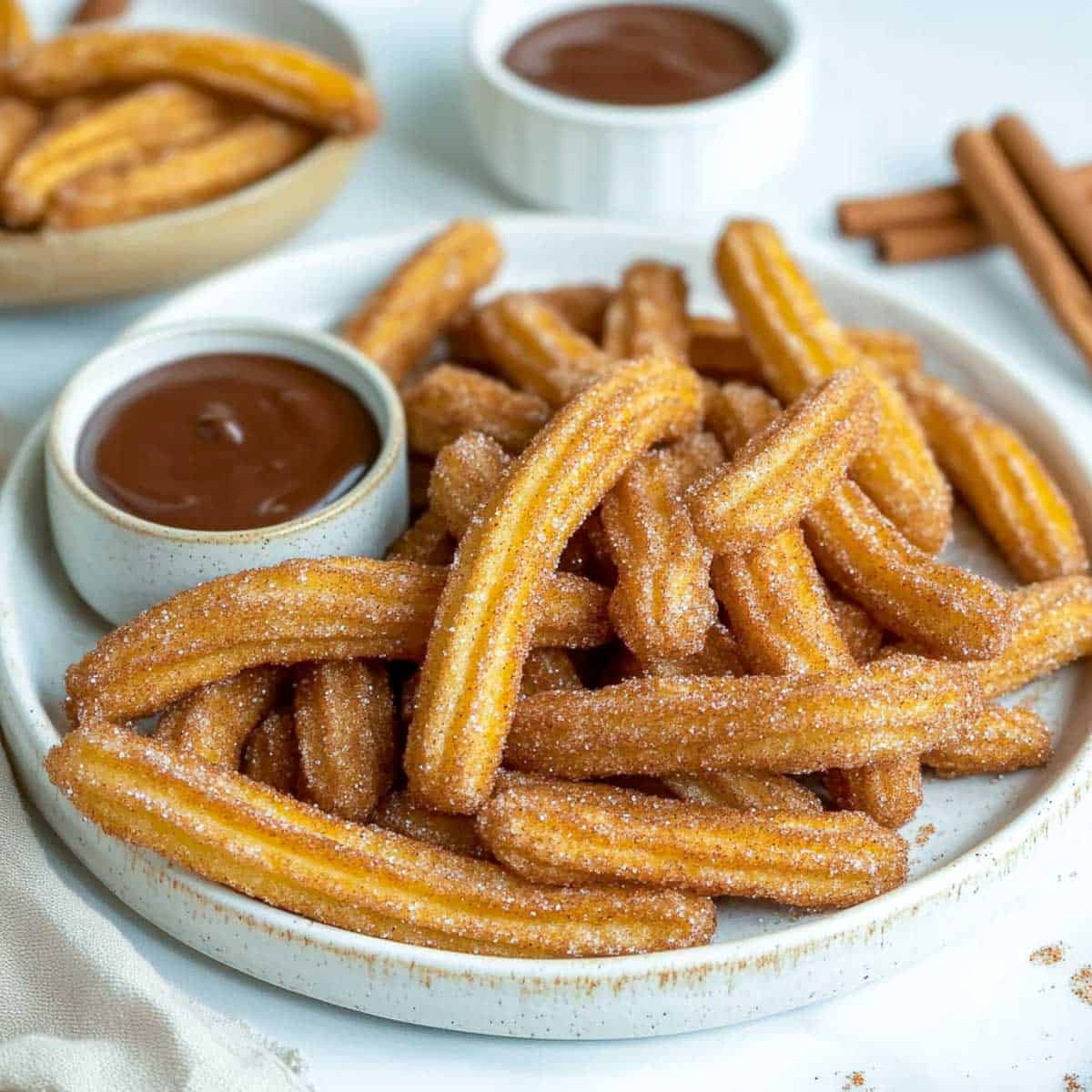 Churros on a plate served with chocolate sauce for dipping.
