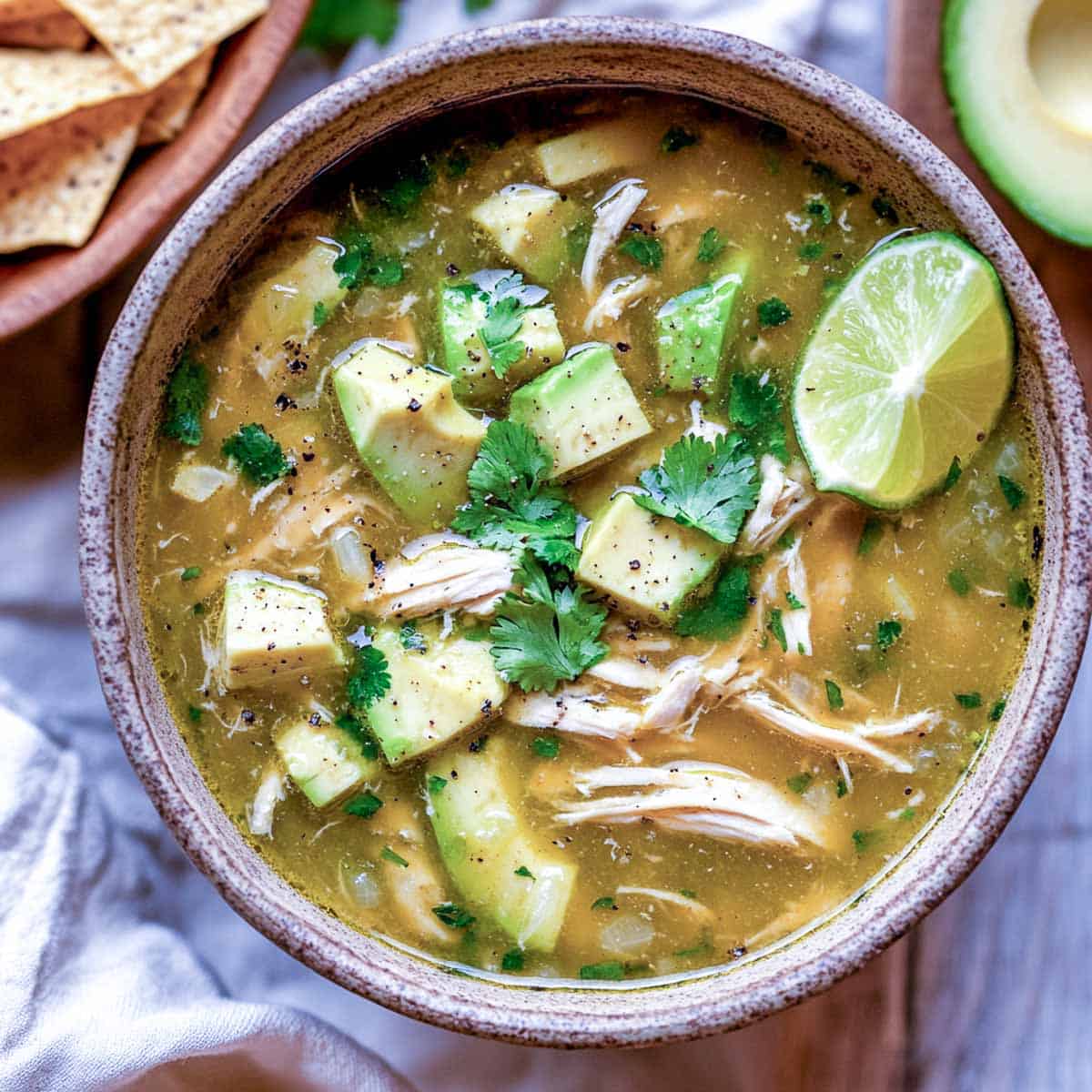 Chicken and avocado soup garnished with lime wedge and served with tortilla chips.