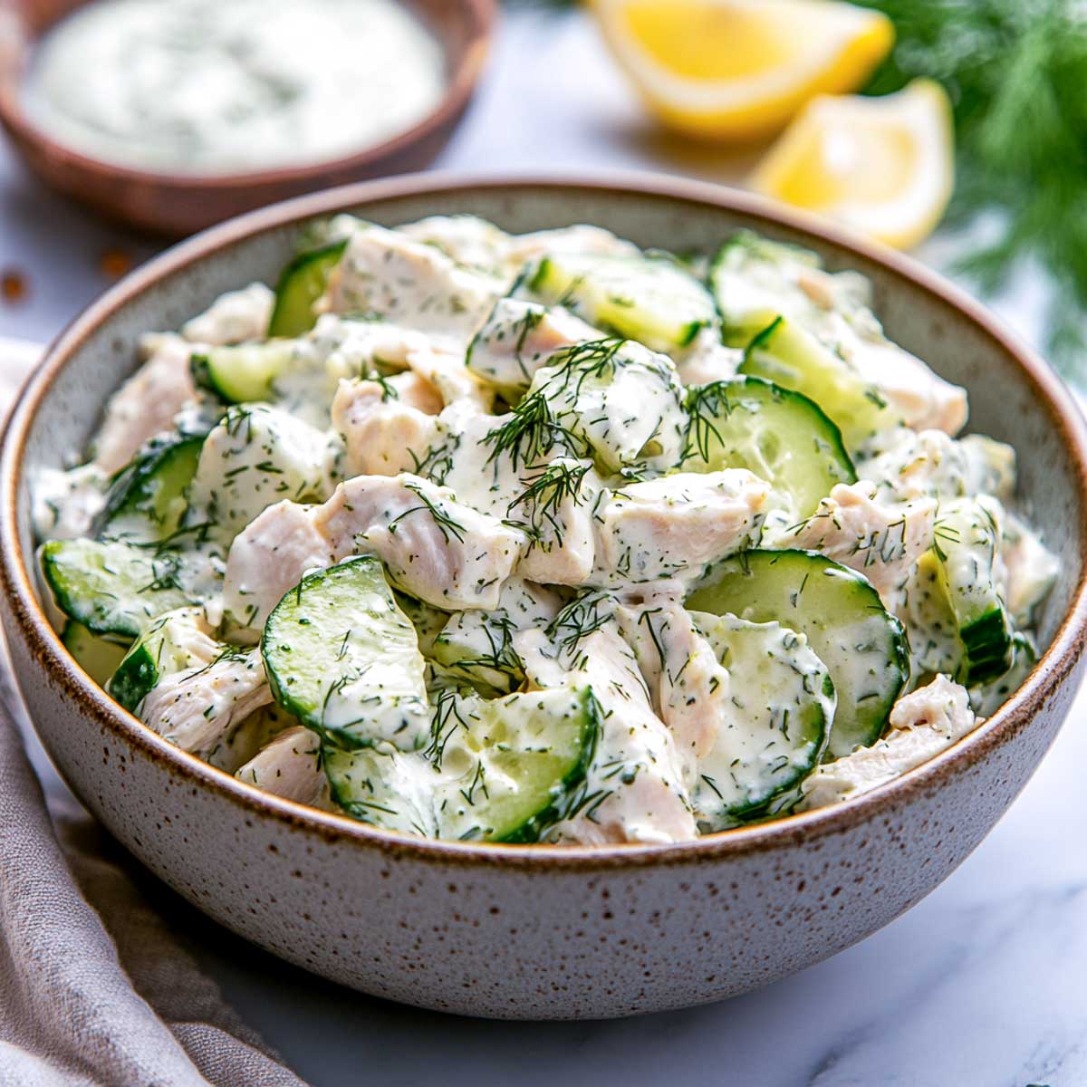 Side view of cucumber dill salad with extra dressing in the background.