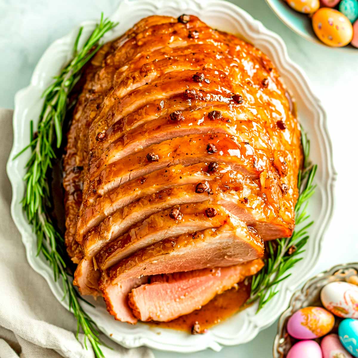 Easter ham on a serving plate with Easter eggs in the background.