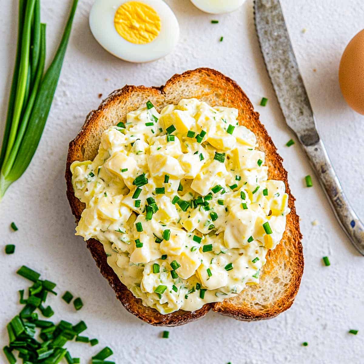 Egg salad spread on a toasted bread and placed on a white surface.