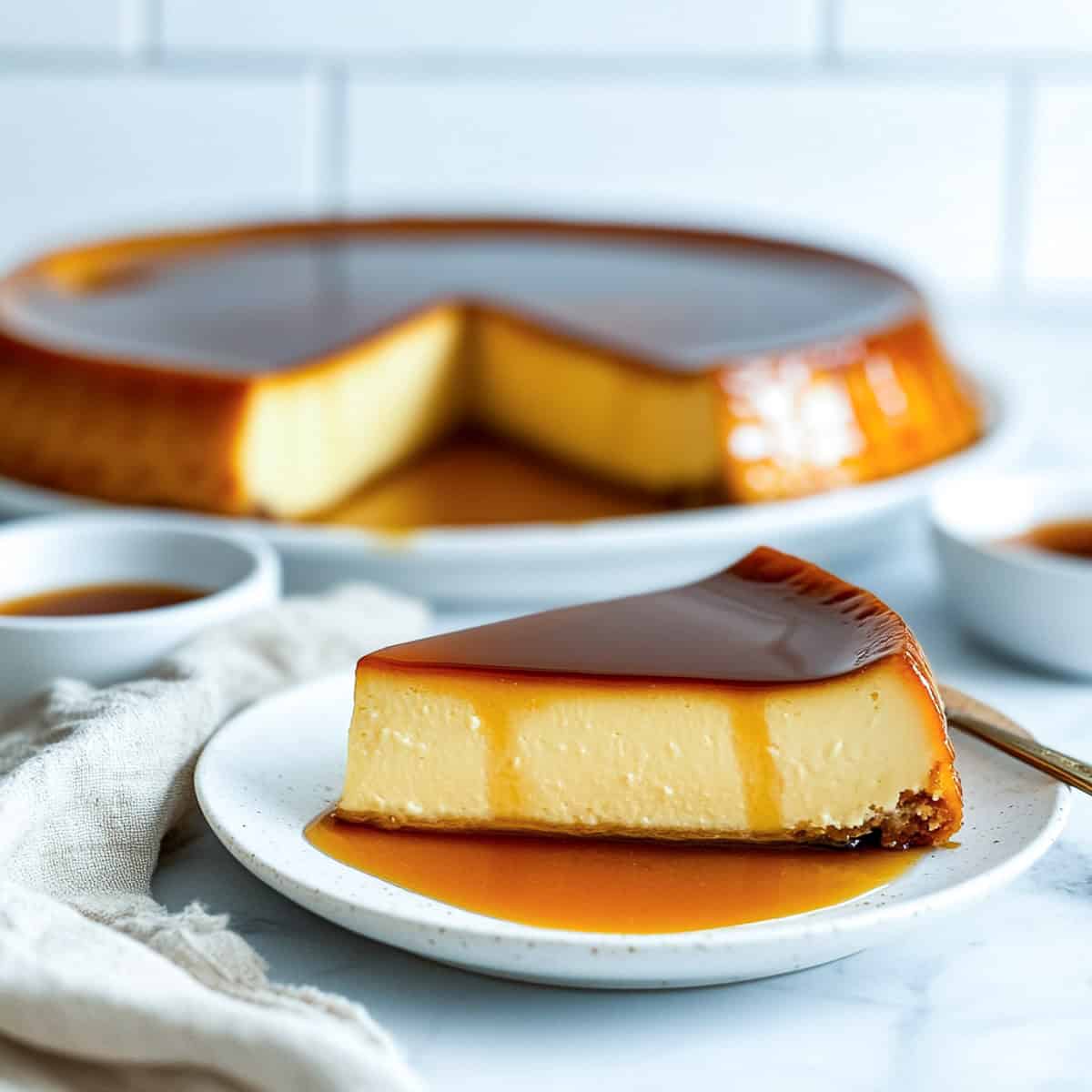 A slice of flan napolitano on a serving plate with the remaining flan in the background.