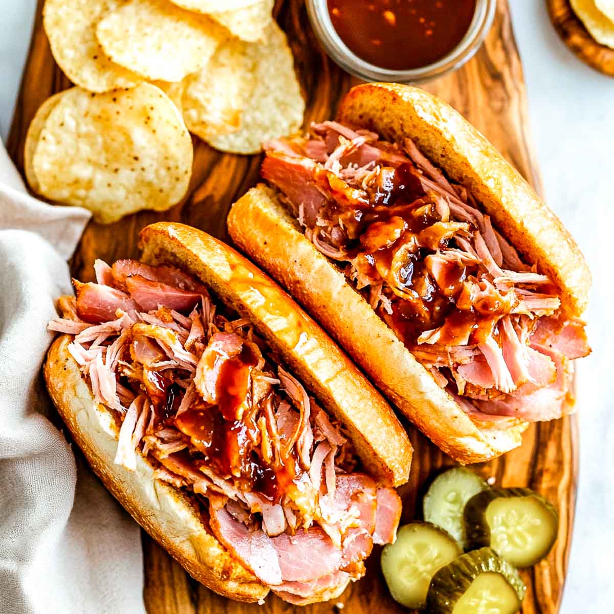 Ham sandwiches placed on a wooden board served with chips.