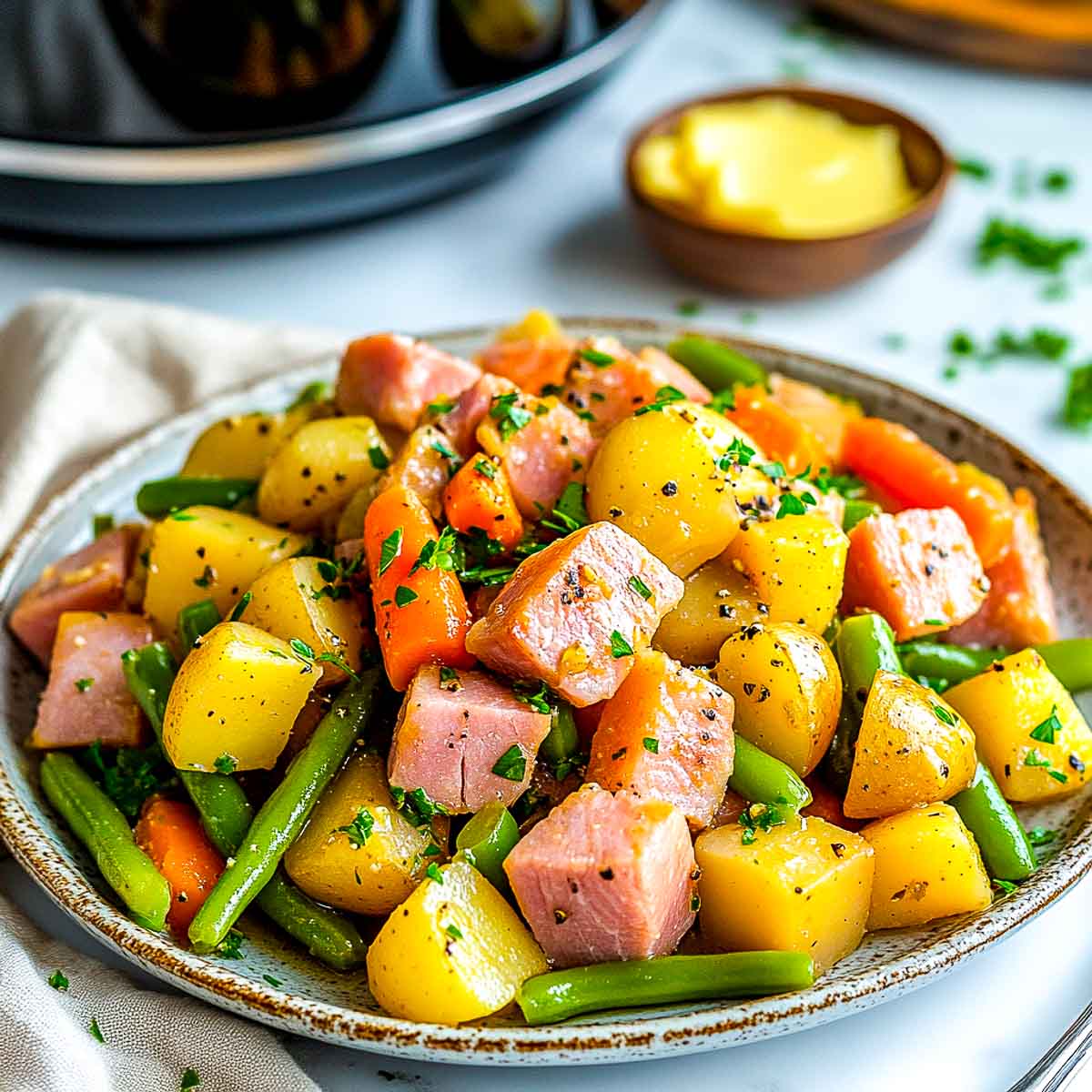 Ham and vegetables on a serving plate with crockpot in the background.
