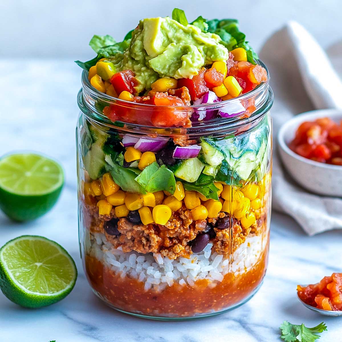 Mason jar burrito bowl on a white marble surface.
