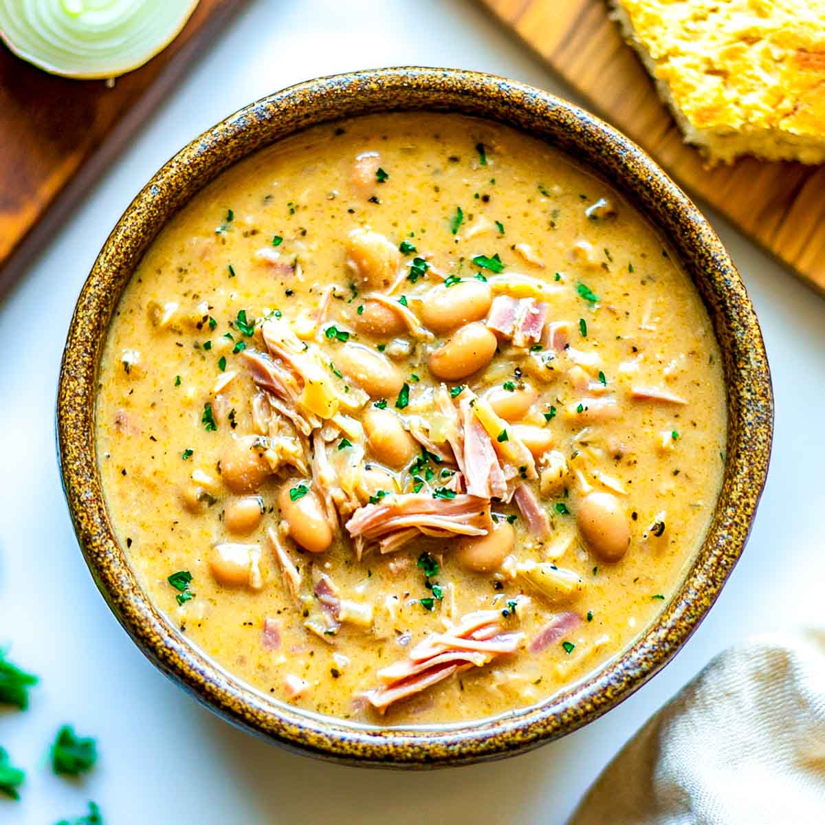 Navy beans and ham served in a brown bowl with bread in the background.