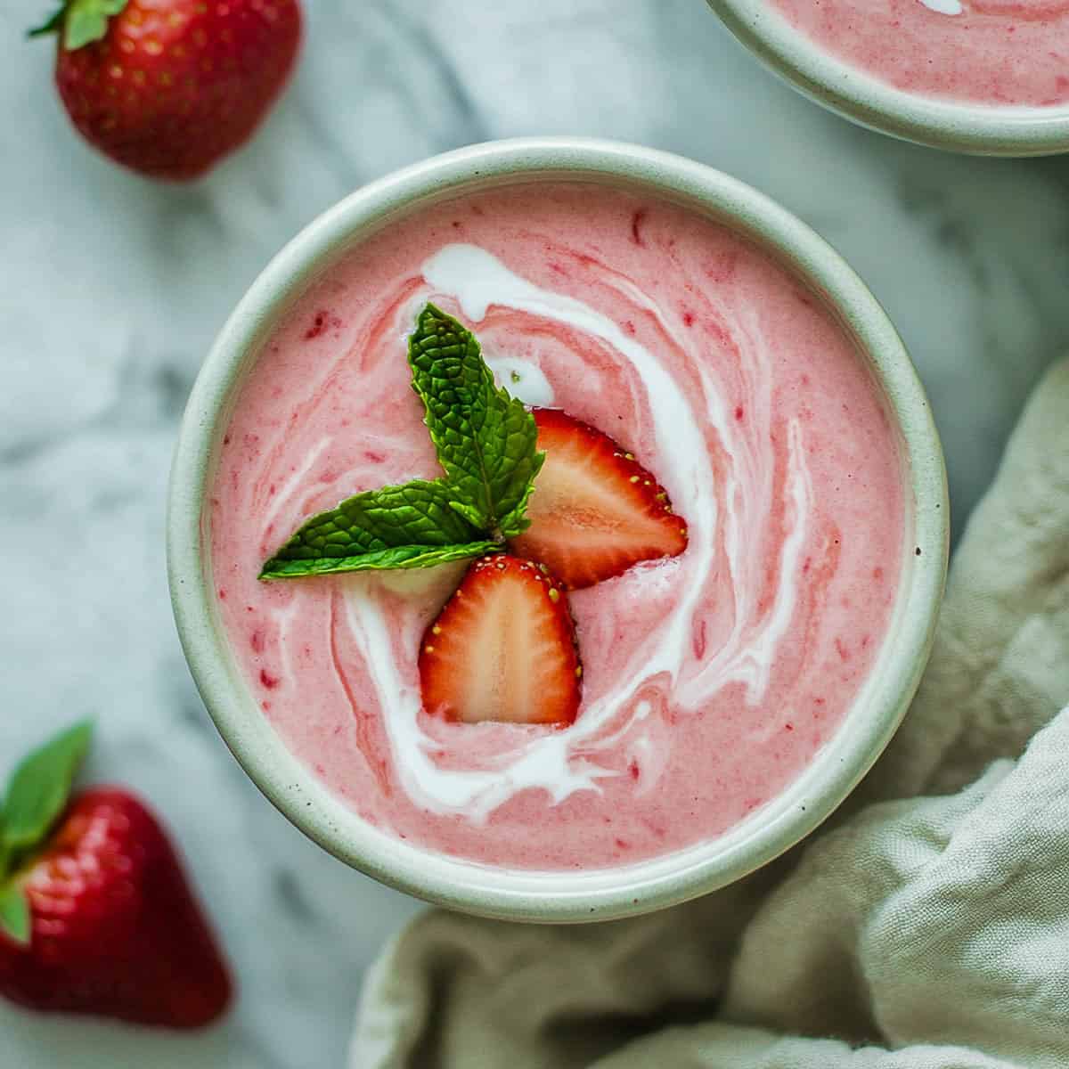 Rhubarb strawberry soup bowls on a white marble surface.