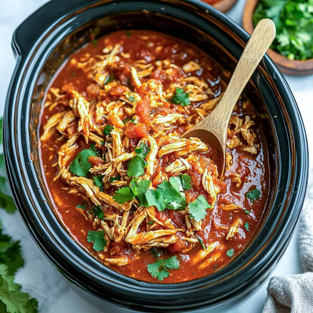 Shredded salad chicken in the crocpot garnished with cilantro.