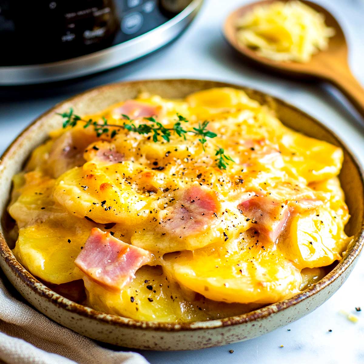 Scalloped potatoes and ham served on a plate with crockpot in the background.