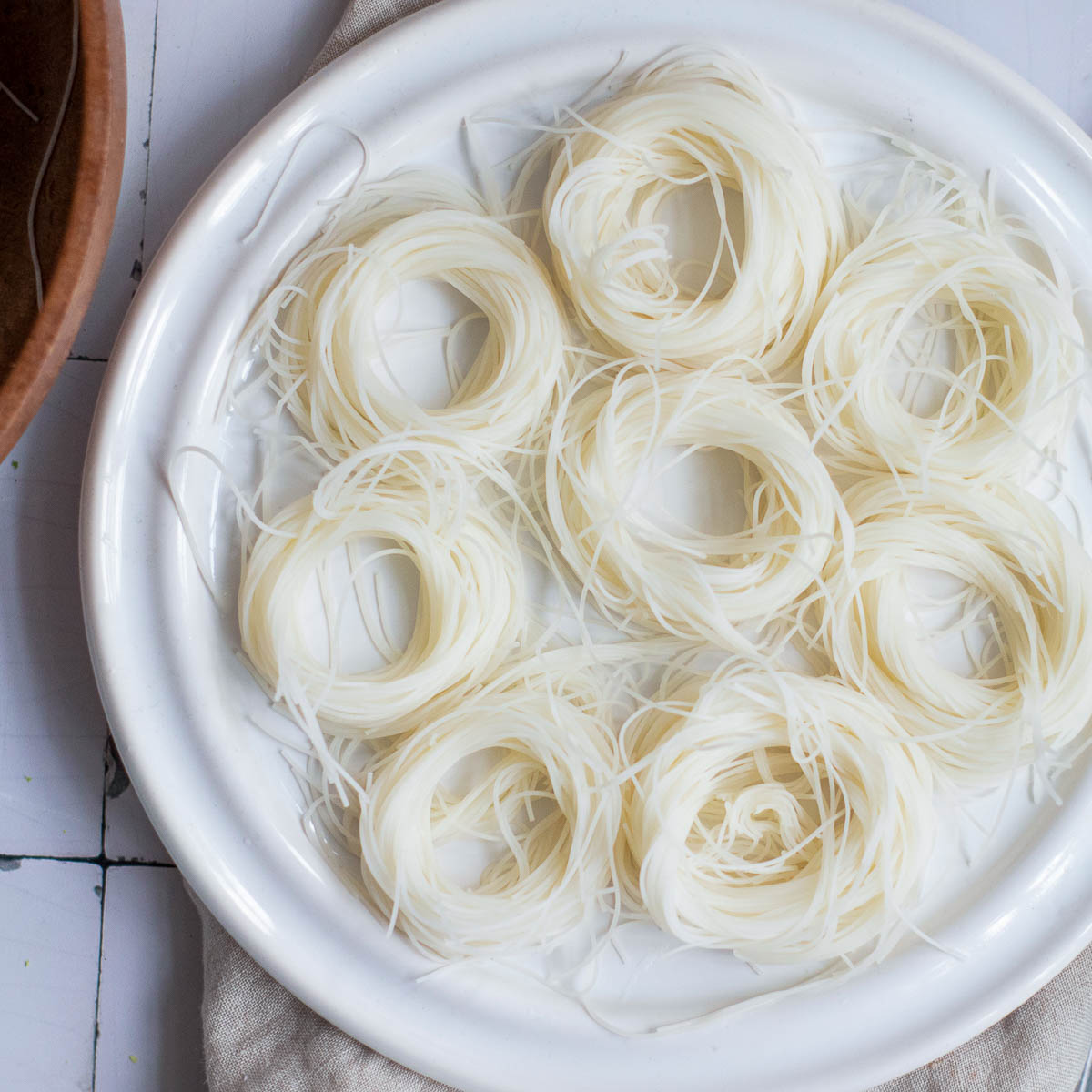 Rice noodles shaped into nests are placed on a white plate.