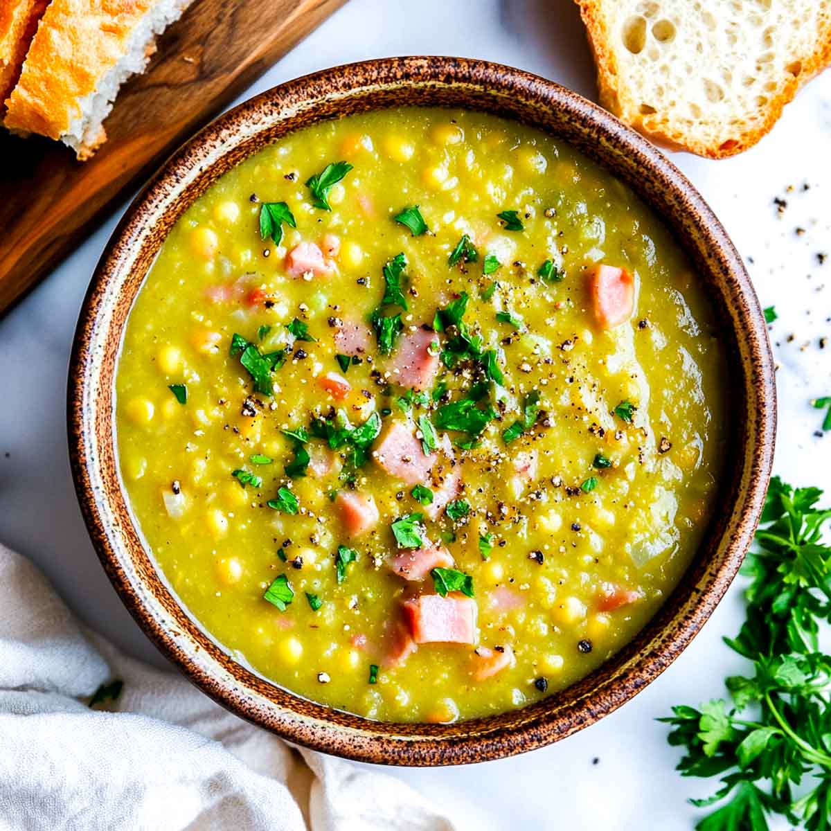 Crockpot split pea ham soup served in a wide bowl with bread in the background.