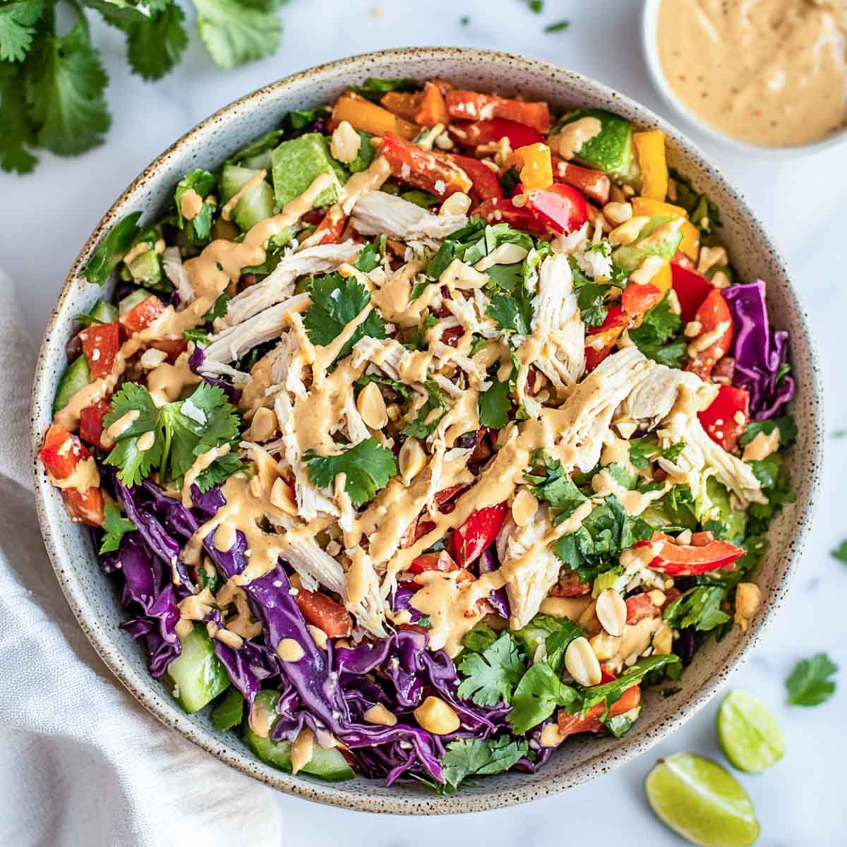Top view of Thai chicken salad in a wide bowl with extra dressing in the background.