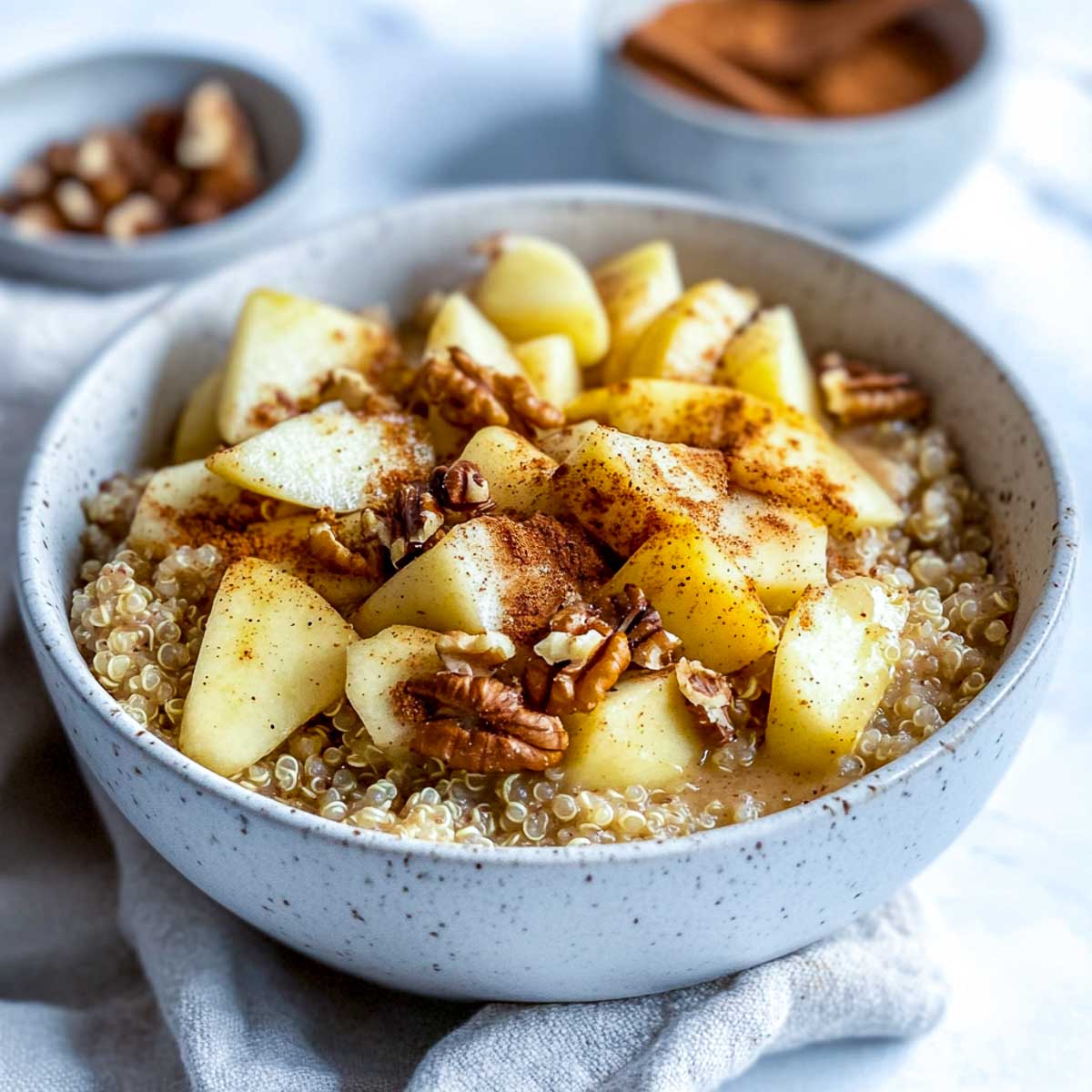 A warm apple cinnamon quinoa bowl topped with diced apples, walnuts, and a sprinkle of cinnamon, served in a white ceramic bowl on a white marble surface.