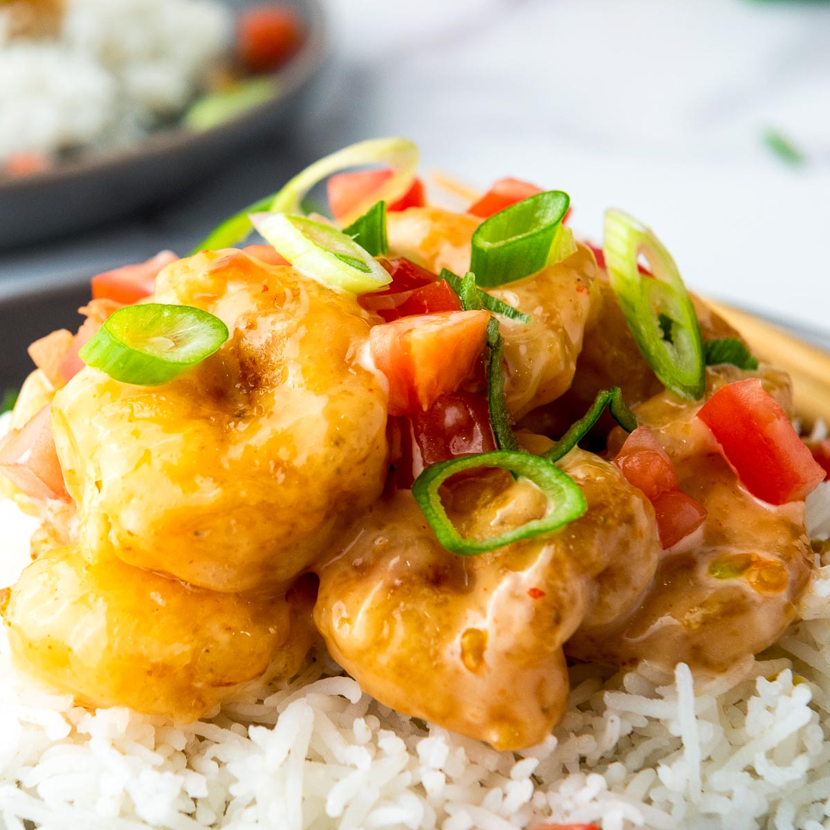 Close up of bang bang shrimp garnished with tomatoes and green onions.
