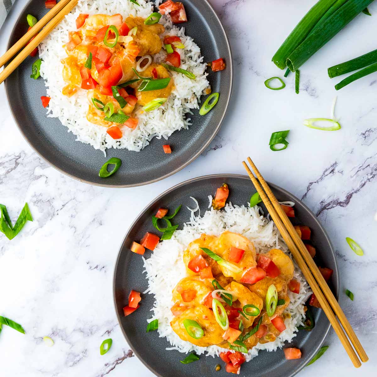 Two plates of bang bang shrimp and rice on black plates placed on a marble surface.