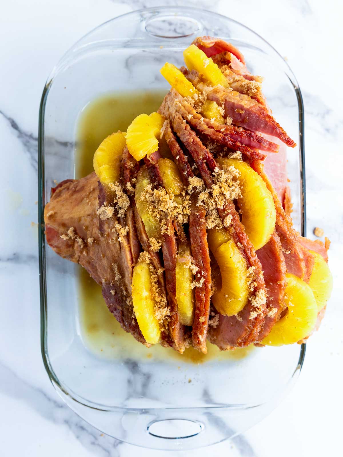 Ham rubbed with brown sugar and pineapple slices in a baking dish.