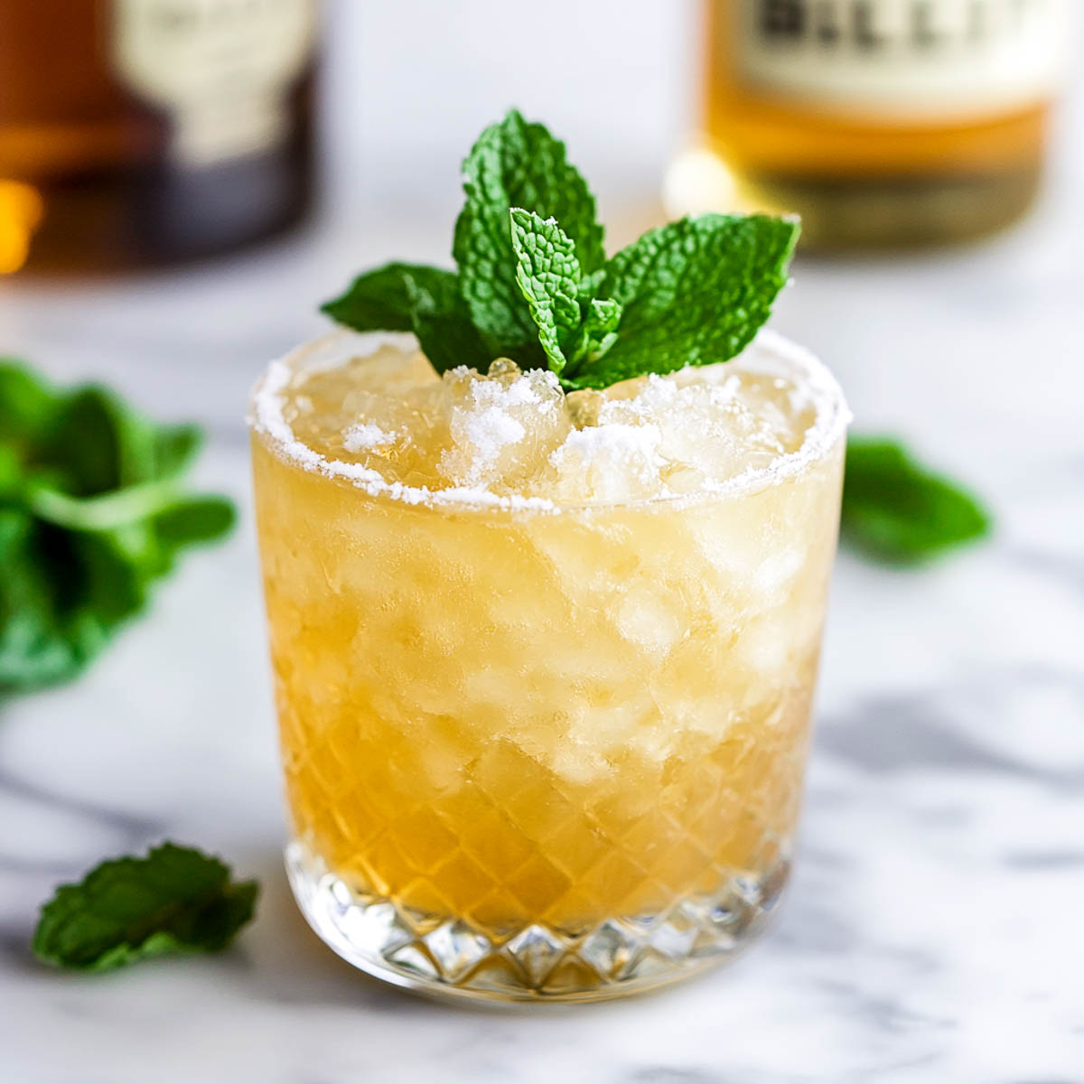 Bulleit Bourbon mint julep garnished with a mint leaf and placed on a white marble surface.