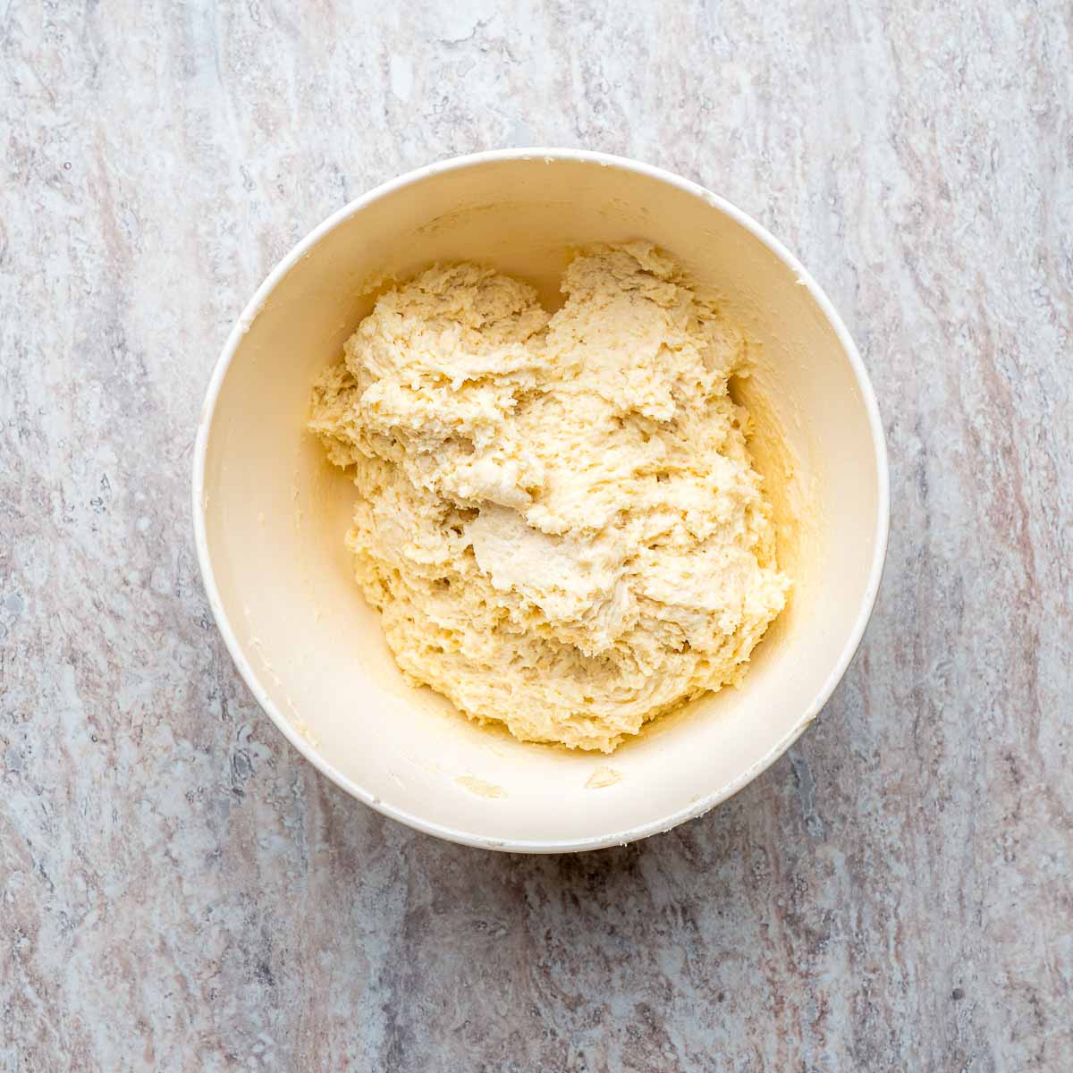 Dough in a mixing bowl placed on a wooden surface.
