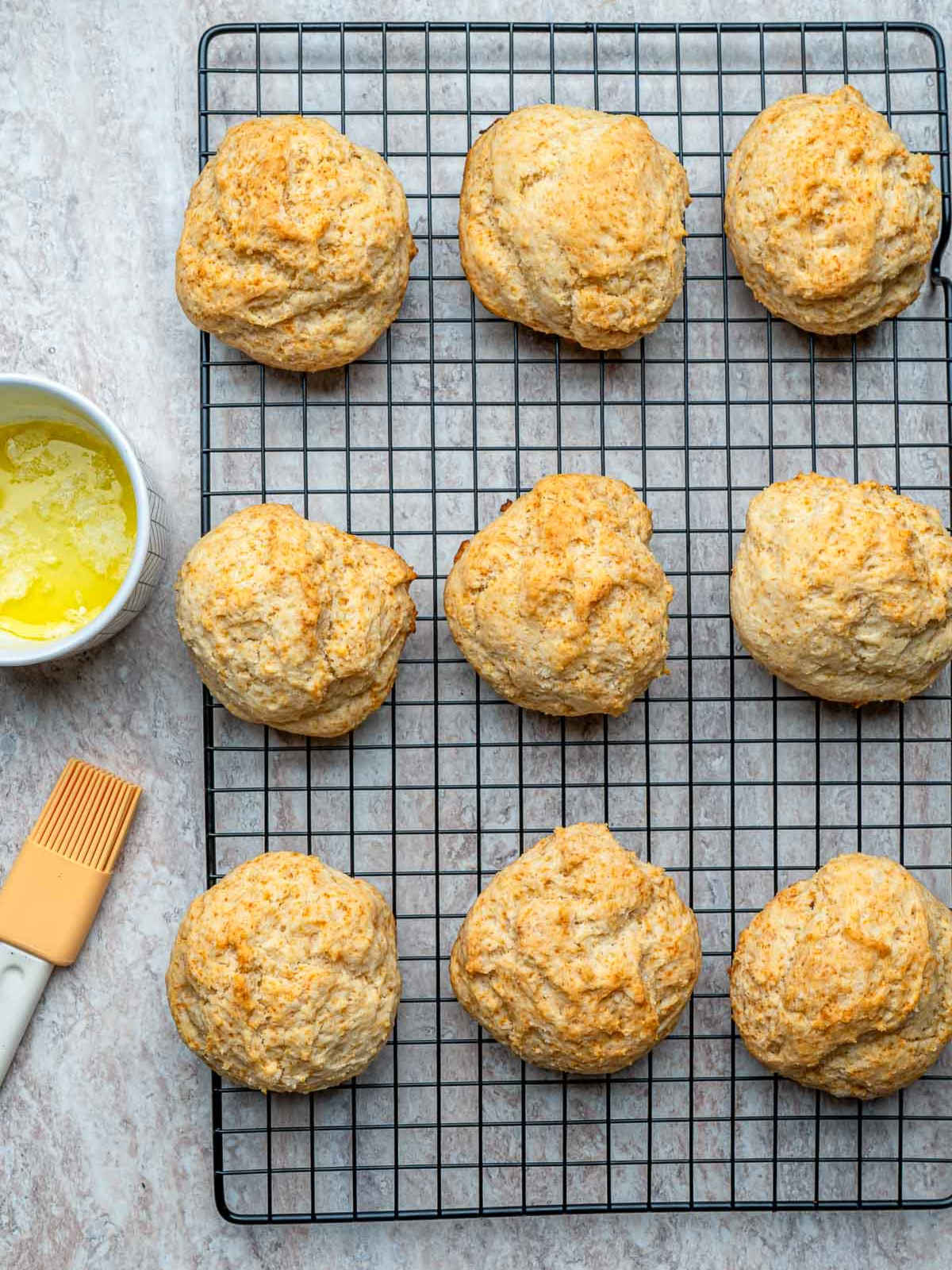 Baked biscuits brushed with butter and cooling on a wire rack.