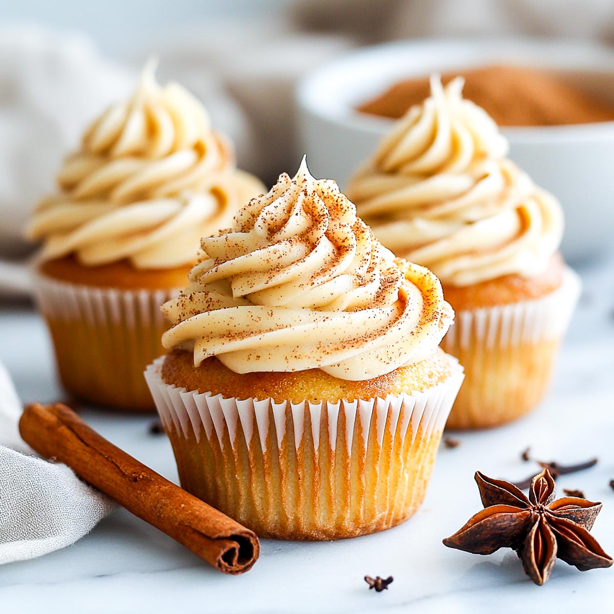 Chai spiced cupcakes on a white marble surface with a bowl of chai spice mix in the background.
