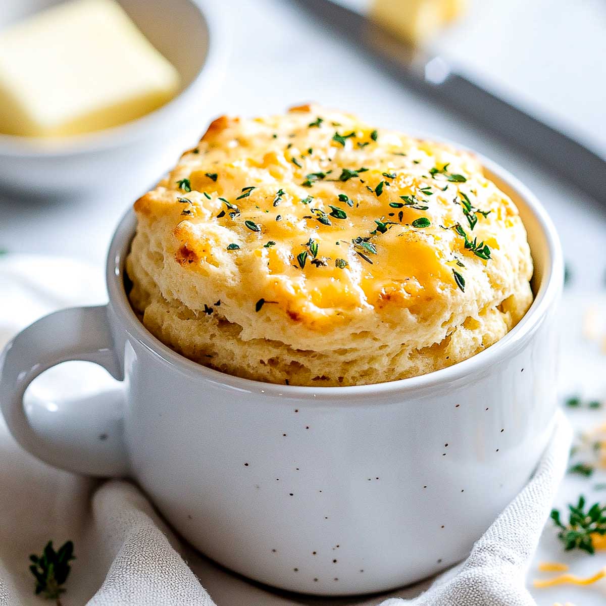 Easy cheddar biscuit made in a mug with butter in the background.