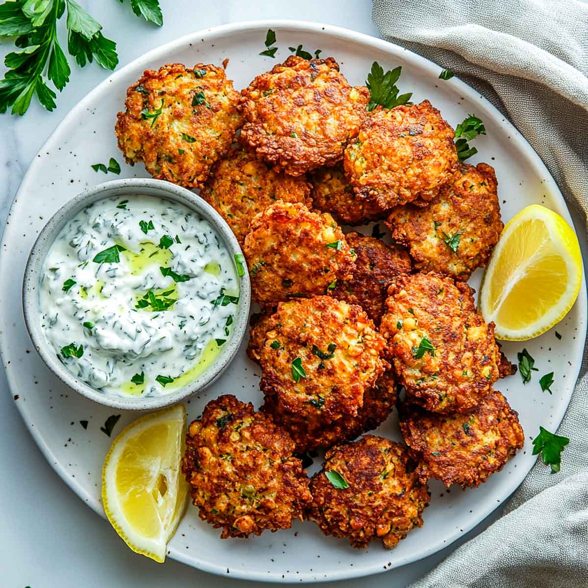 Crispy fritters on a white plate served with yogurt sauce.