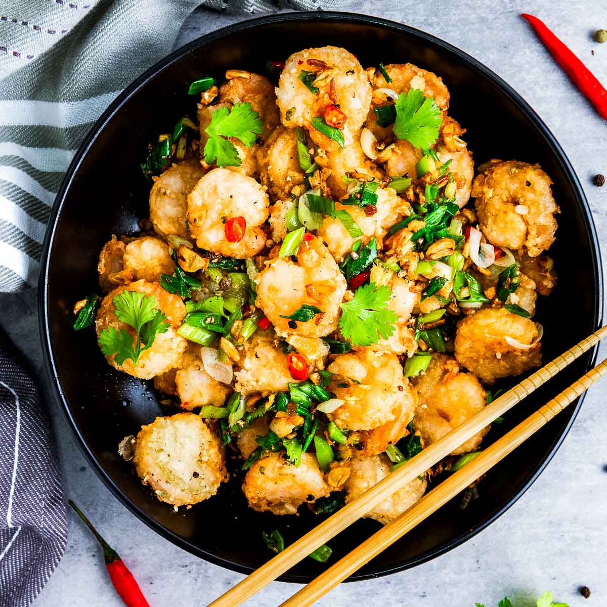 Salt and pepper shrimpa in a black plate with chopsticks in the side.