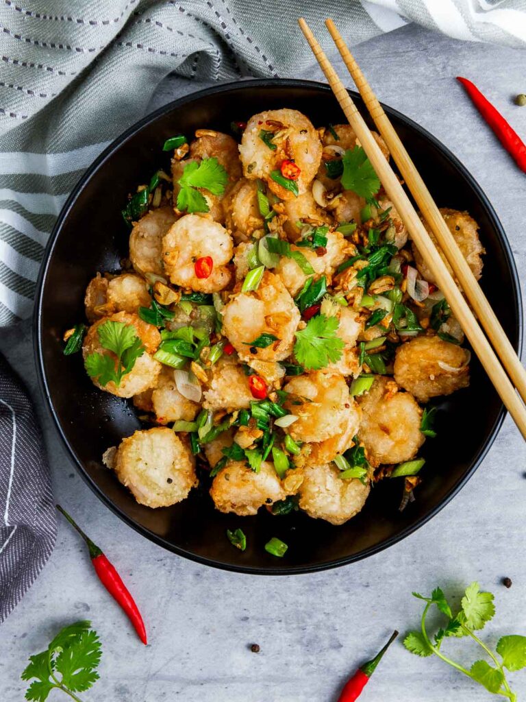 A bowl of salt and pepper shrimp on a grey surface with Thai chili peppers in the backfround.
