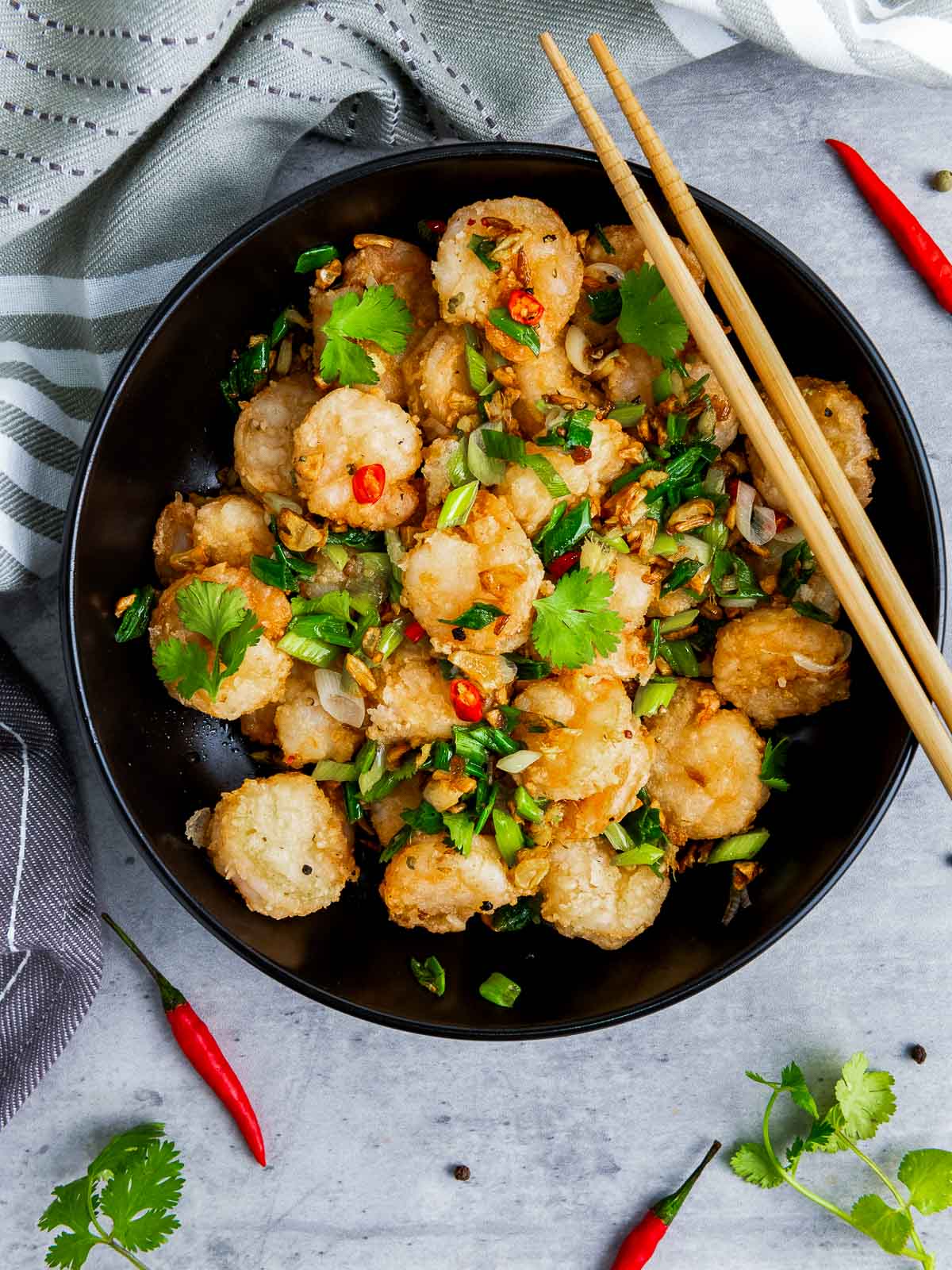 A bowl of salt and pepper shrimp on a grey surface with Thai chili peppers in the backfround.