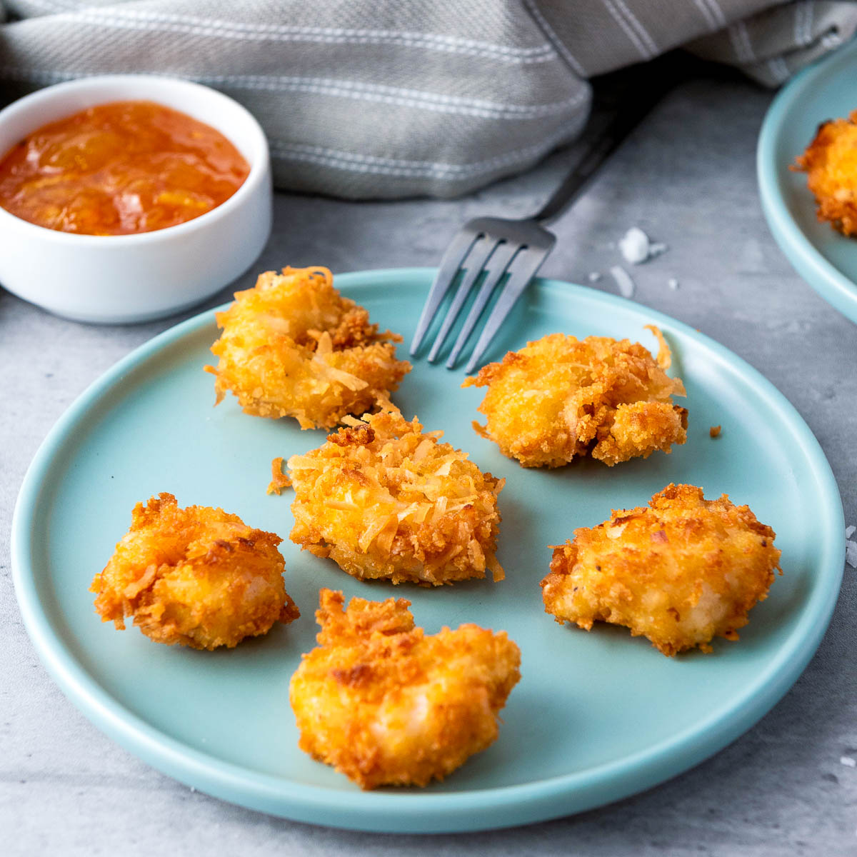 Side view of a plate of coconut shrimp with chili orange sauce in the background.