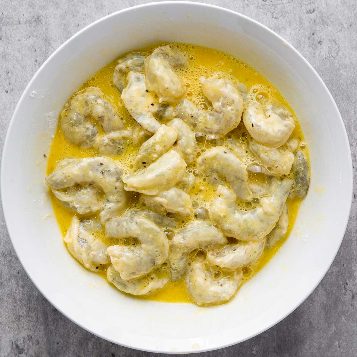 Shrimp dipped in eggs in a wide bowl.