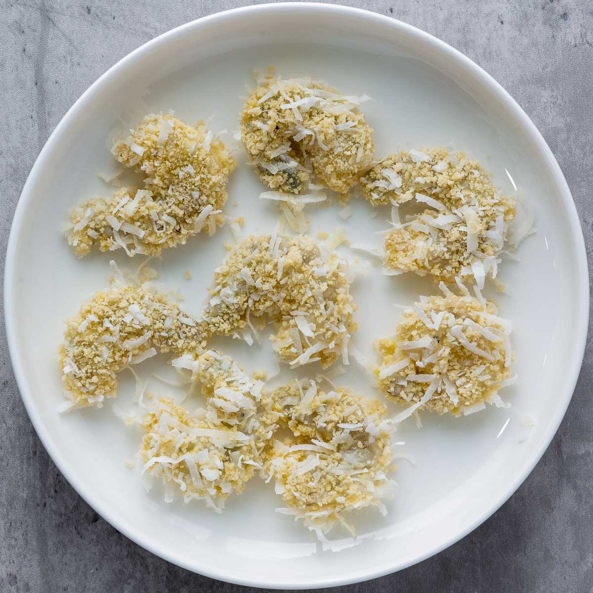 Coated shrimp placed on a white plate to set.