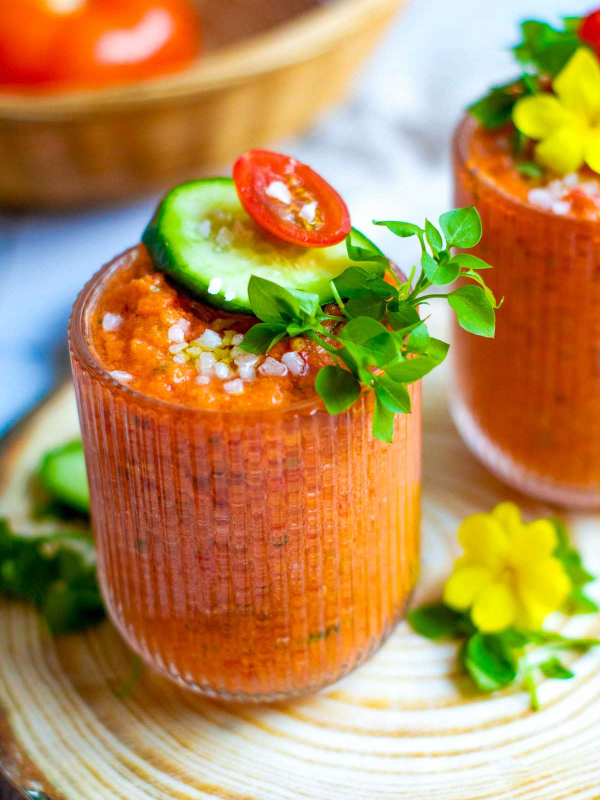 A glass of gazpacho shot topped with cucumber slice and microgreens.