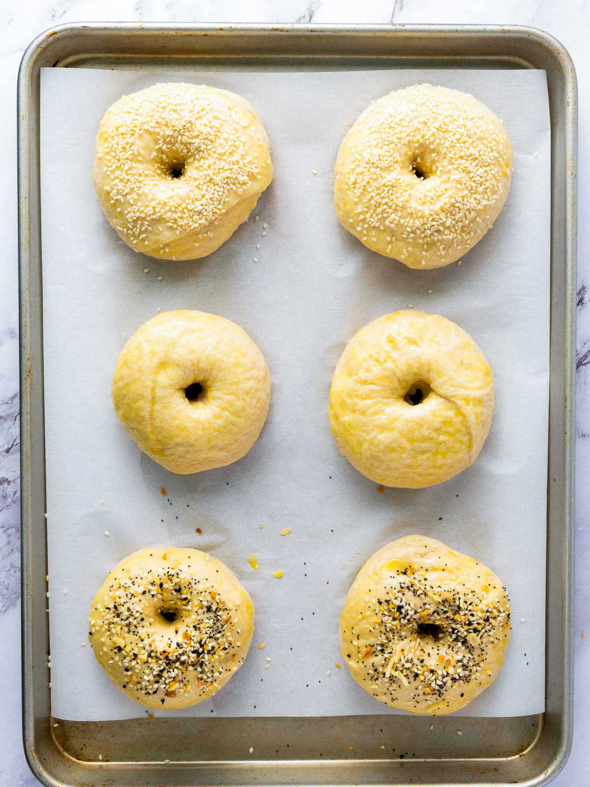 Boiled dough balls on a baking tray topped with egg wash and seasoning.