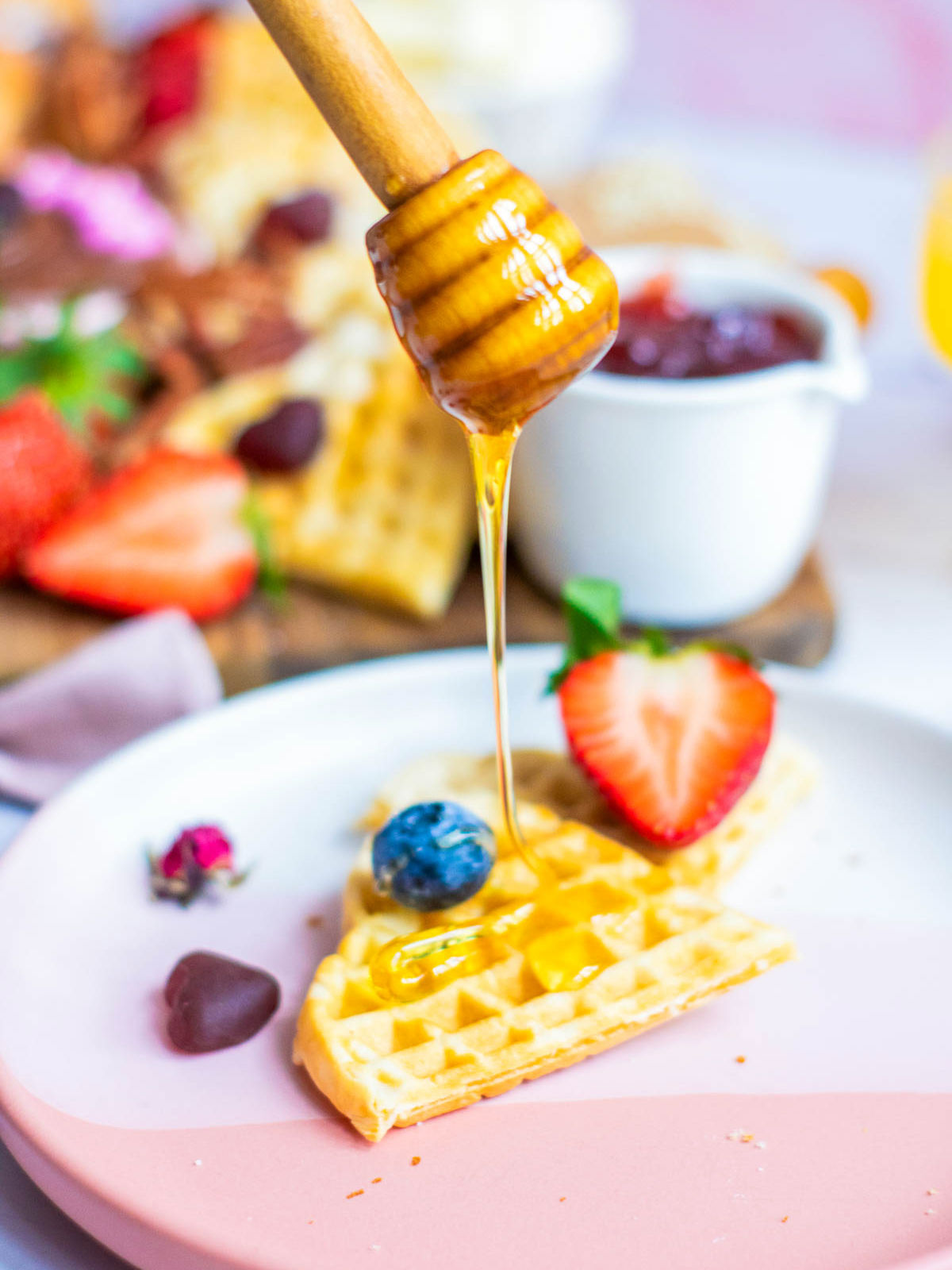 Waffle on a pink serving plate being topped with honey.