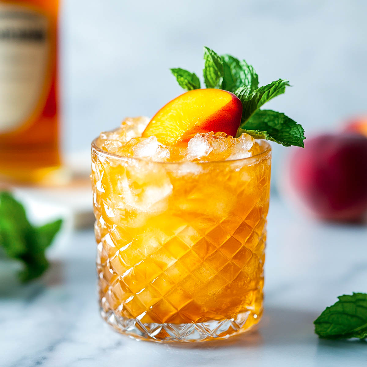 Peach Bourbon smash in a rocks glass with a whiskey bottle in the background.